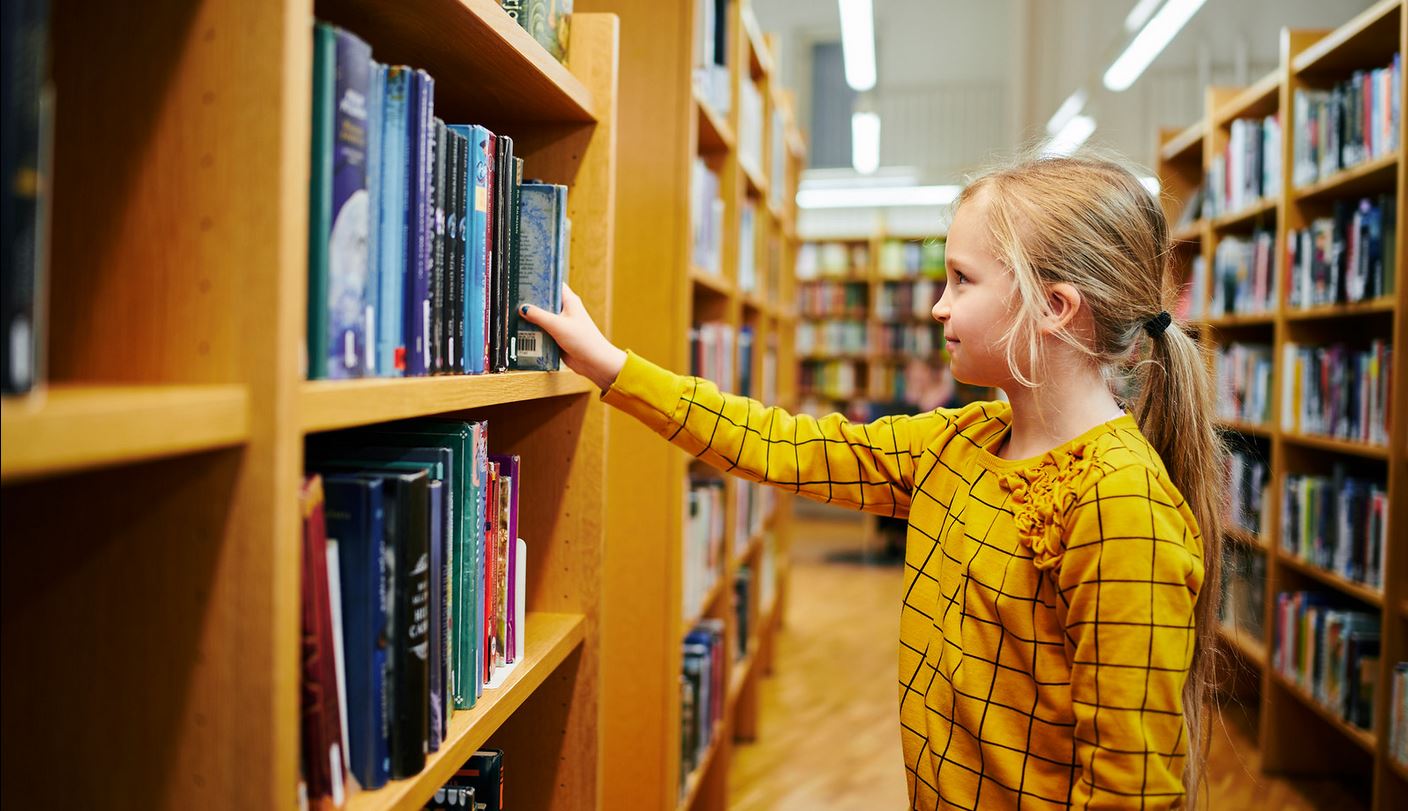 Tyttö ottaa kirjaa kirjaston hyllystä